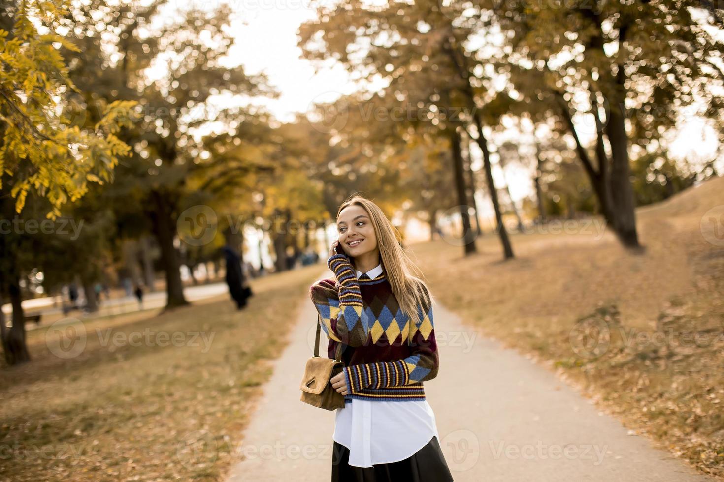 bela jovem caminhando no parque outono e usando um telefone celular foto