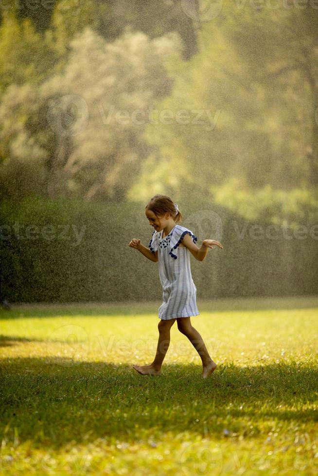 garotinha fofa se divertindo sob o aspersor de irrigação foto