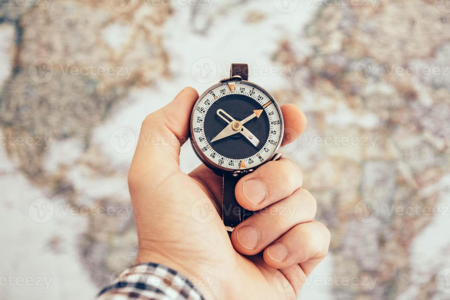 mão de homem segurando uma bússola vintage com mapa-múndi como pano de fundo foto