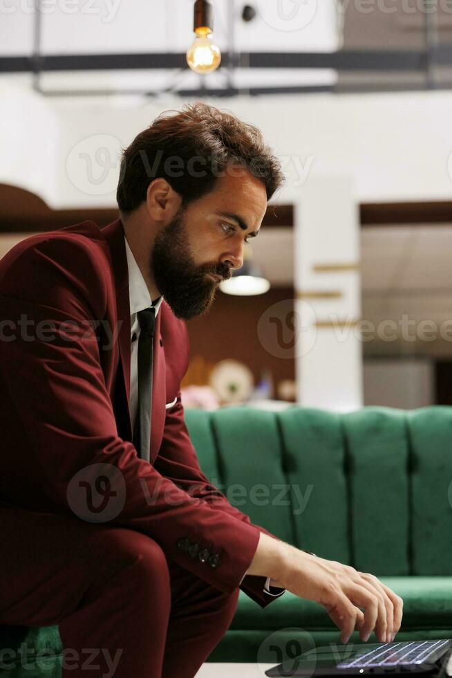 branco colarinho trabalhador dentro hotel salão usando computador portátil para Reveja Novo discurso notas, preparando para importante o negócio conferência. jovem adulto esperando para Verifica dentro às recorrer, roupa formal. foto