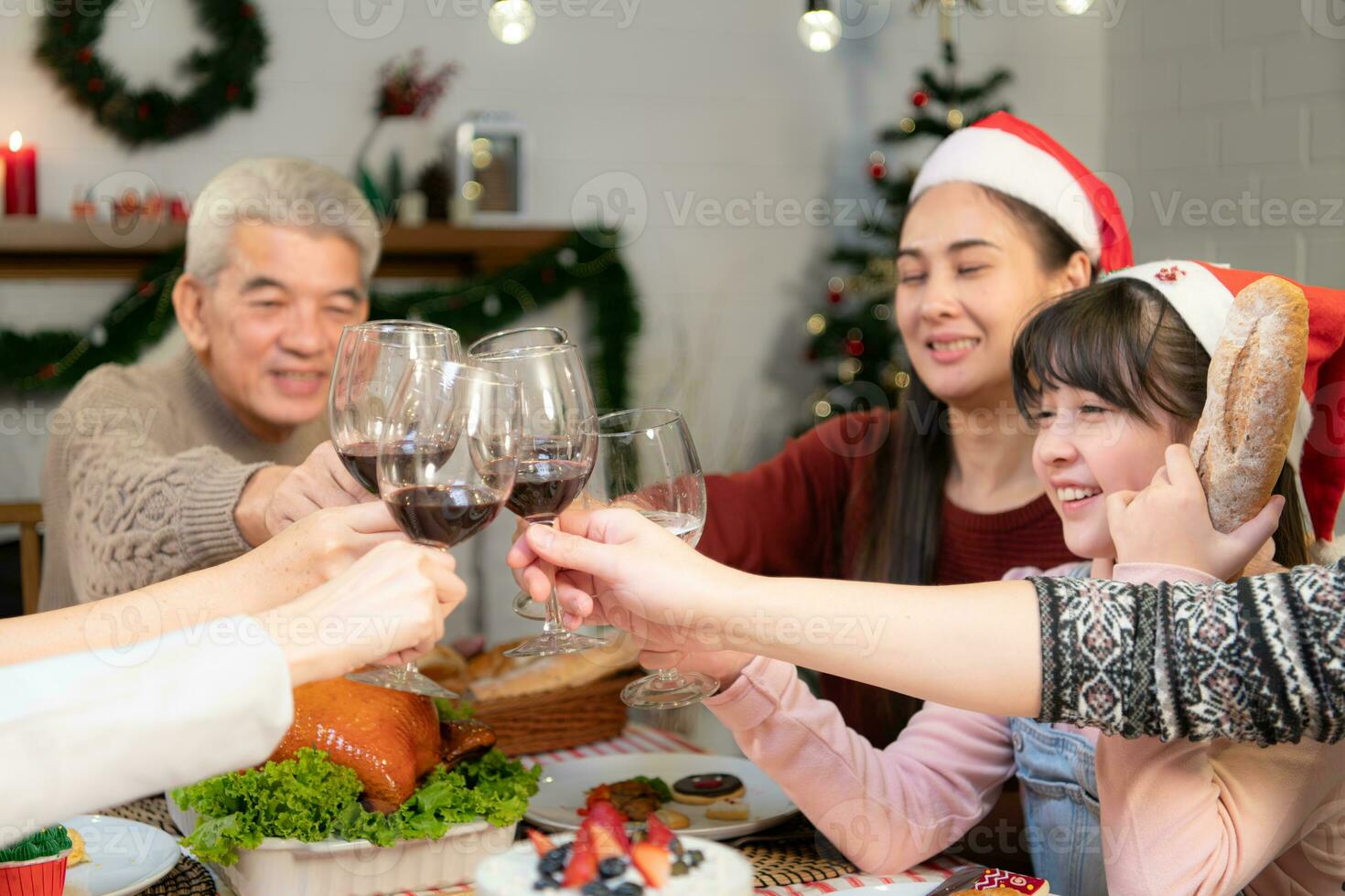 feliz ásia família a comemorar Natal juntos às lar. alegre Senior pais e crianças dentro santa chapéu tilintar óculos do vermelho vinho. foto