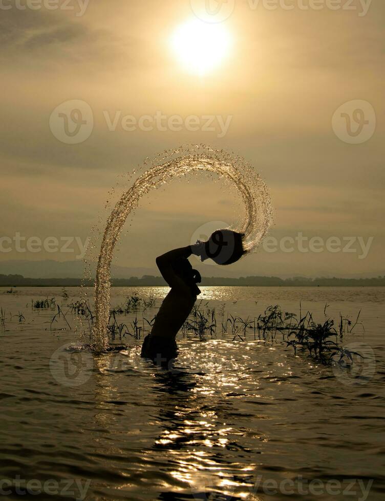 silhueta do uma pescador dentro a água às pôr do sol, tailândia. foto