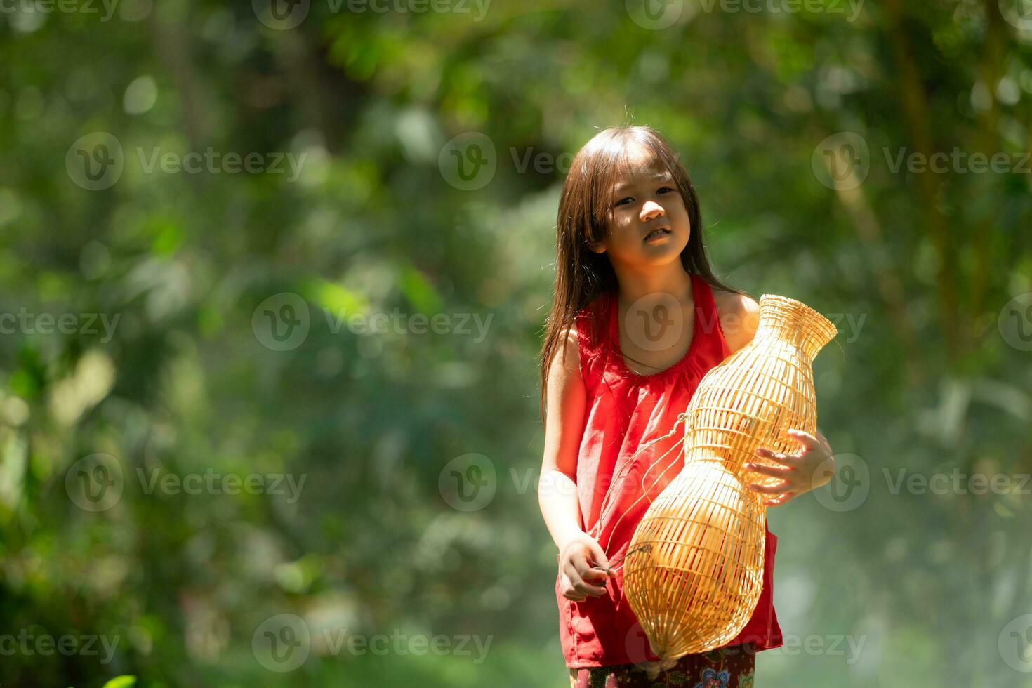 pequeno ásia menina dentro vermelho vestir segurando pescaria equipamento dentro a floresta, rural Tailândia vivo vida conceito foto