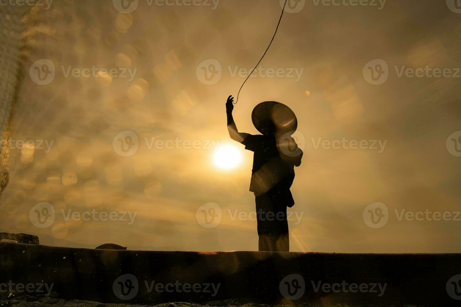 silhueta do pescador às nascer do sol, em pé a bordo uma remo barco e fundição uma internet para pegar peixe para Comida foto