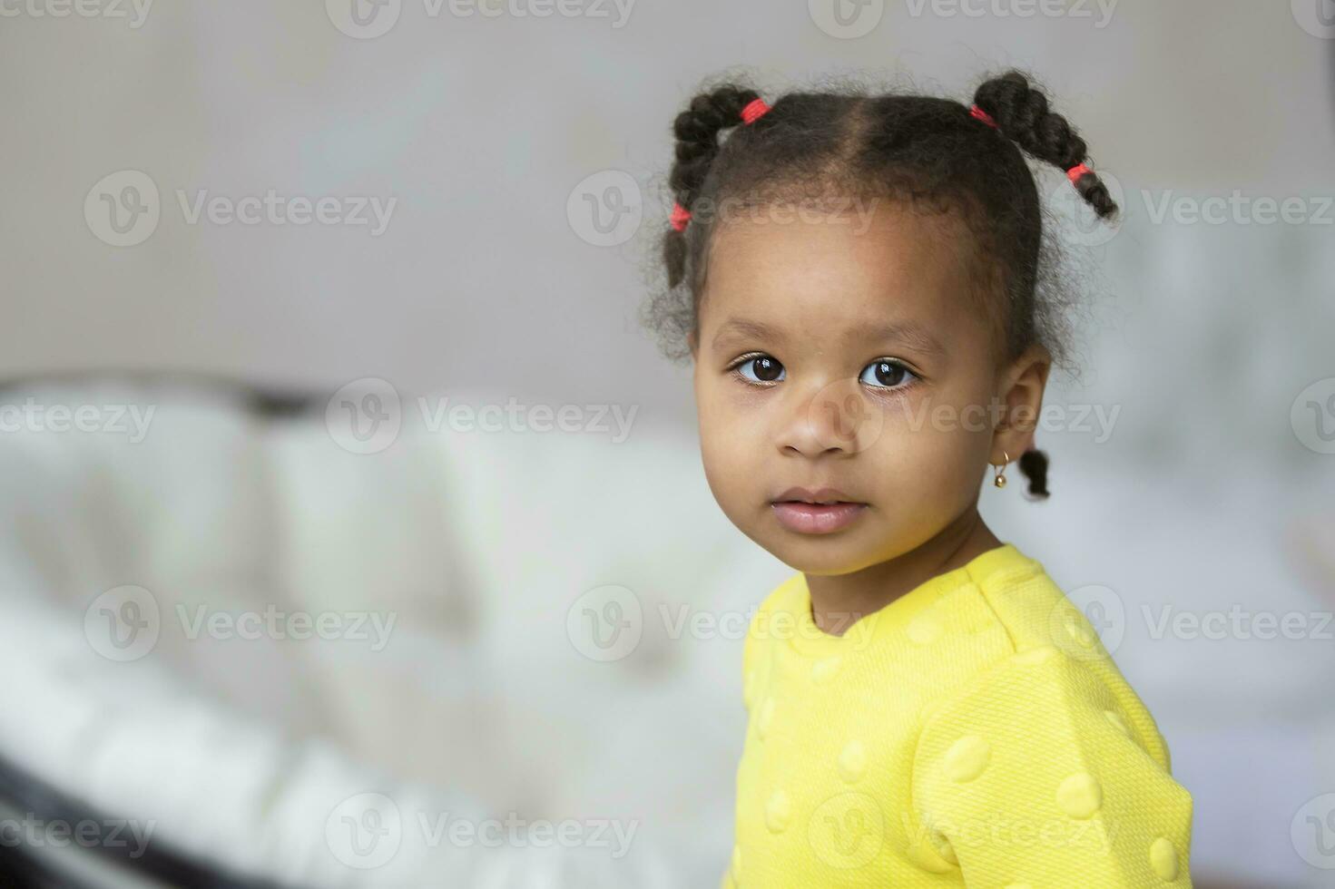 pequeno africano americano menina dentro uma amarelo vestir parece às a Câmera. foto