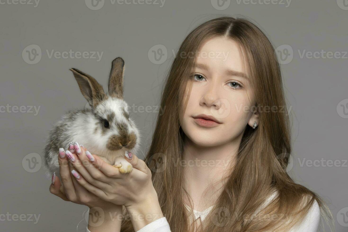 feliz jovem menina segurando uma branco Coelho em uma cinzento fundo foto