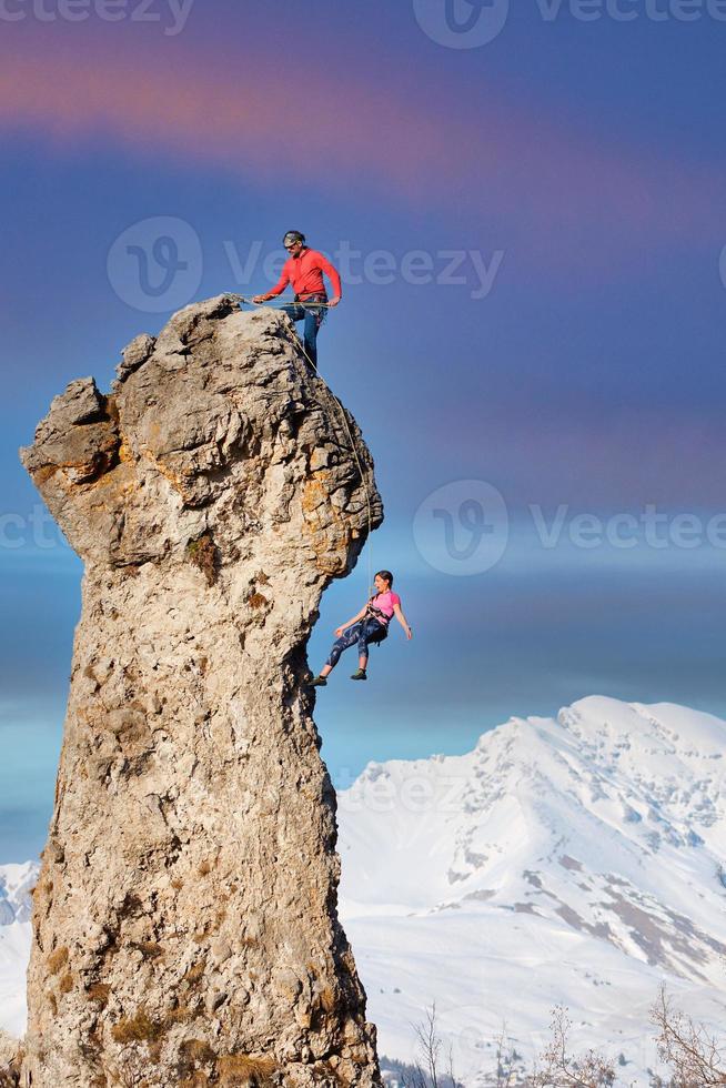 um escalador no topo faz seu parceiro descer a corda foto