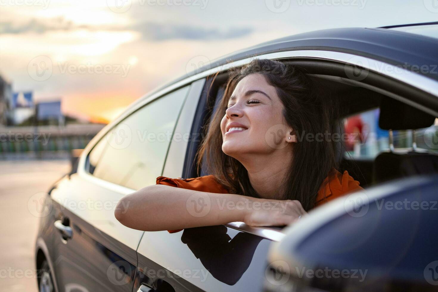 alegre jovem fêmea sentado dentro brilhante carro em passageiro assento e inclinado Fora aberto janela enquanto desfrutando a passeio foto