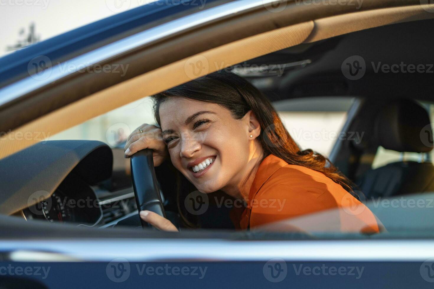 jovem abraçando seu carro novo. jovem animada e seu carro novo dentro de casa. mulher jovem e alegre desfrutando de carro novo abraçando o volante sentado dentro foto