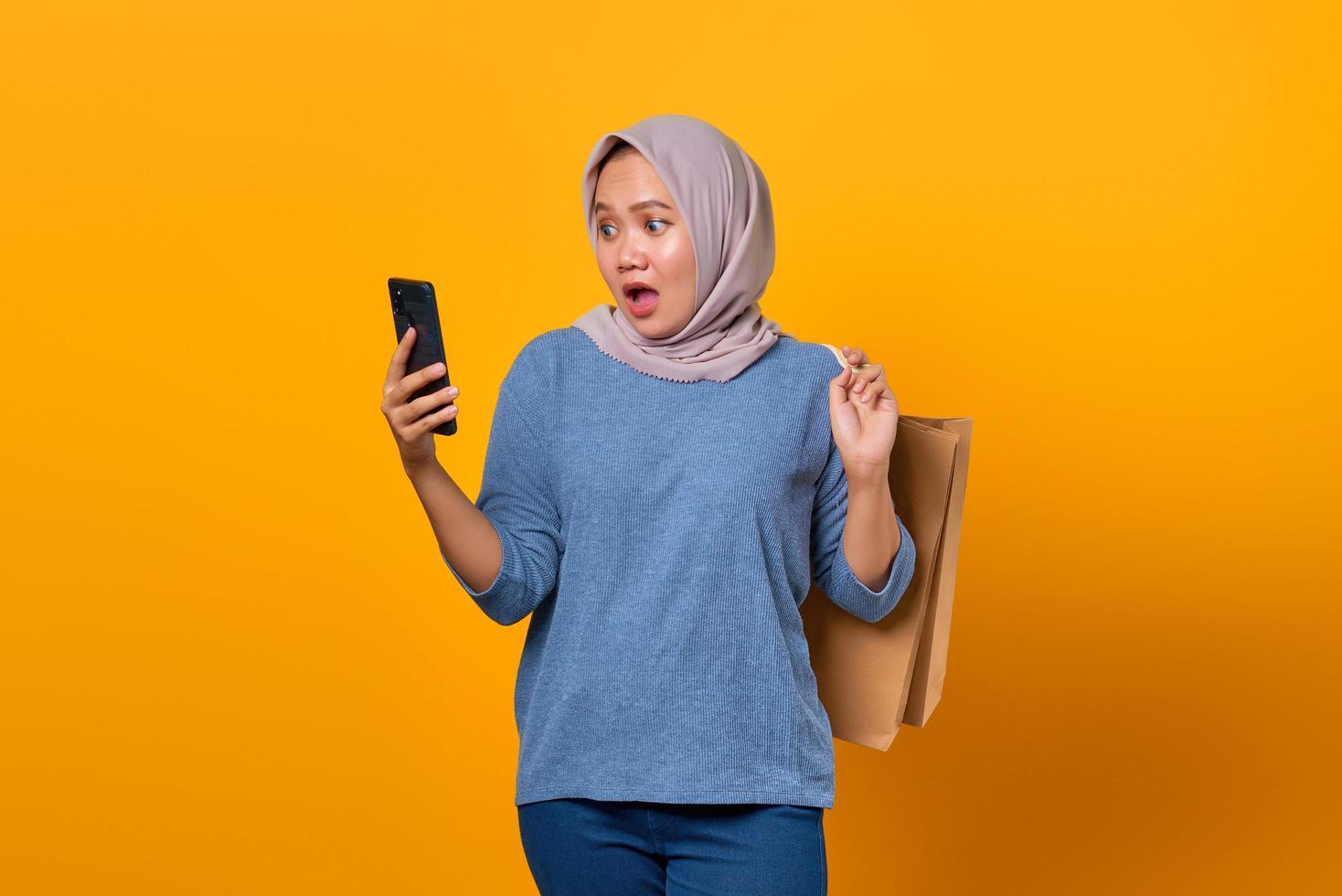 chocada mulher asiática segurando um telefone e uma sacola de compras foto