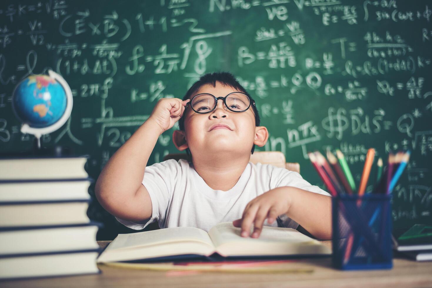 menino pensativo com livro na sala de aula foto