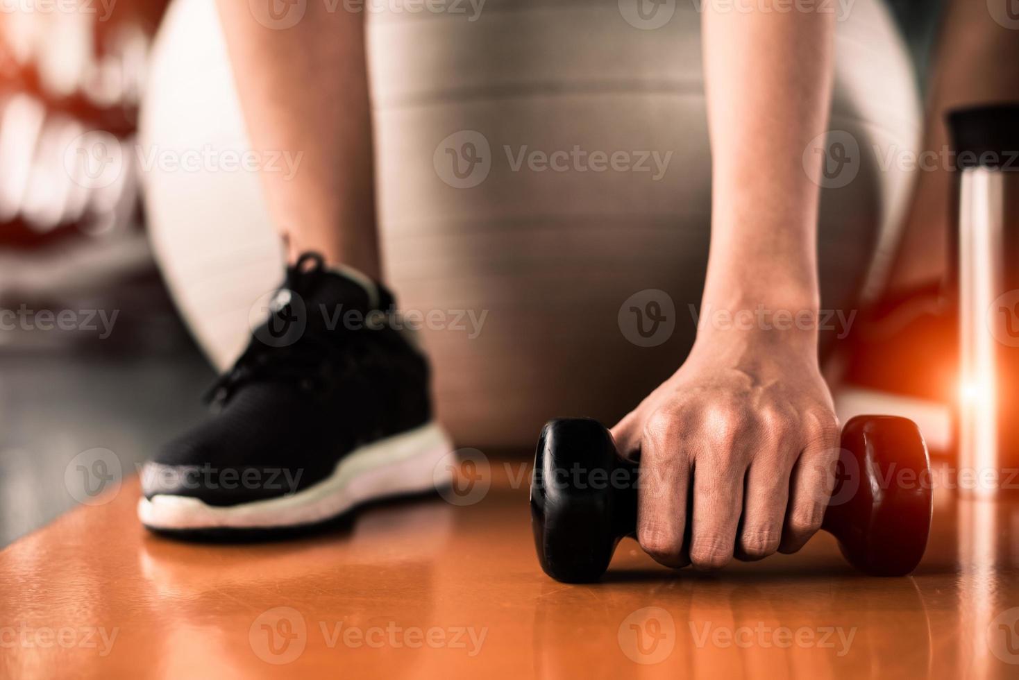 close-up de mulher esportiva sentada na bola de ioga e pegando halteres foto