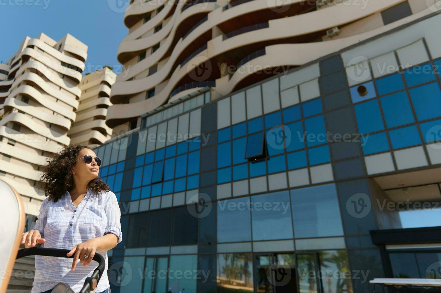 inferior Visão do uma mulher com bebê carrinho de bebê contra Alto subir edifícios fundo foto