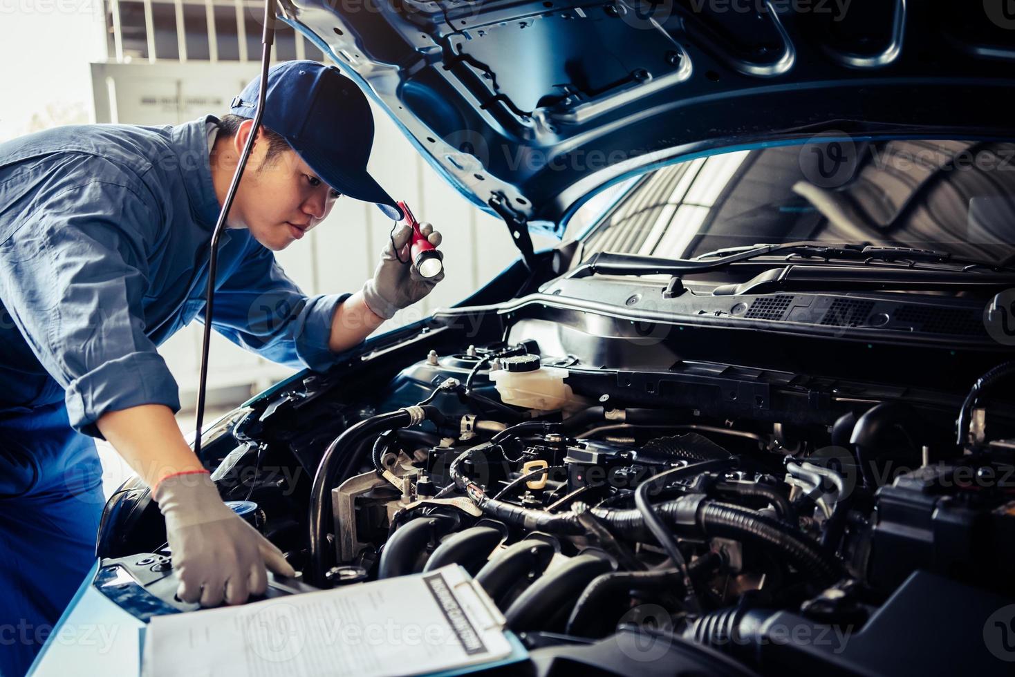 técnico de mecânico de automóveis segurando uma lanterna, verificando o motor foto