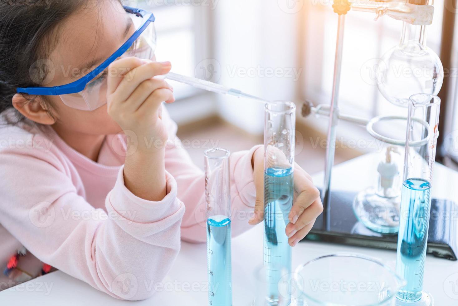 Químico de criança asiática segurando o frasco e o tubo de ensaio nas mãos no laboratório foto