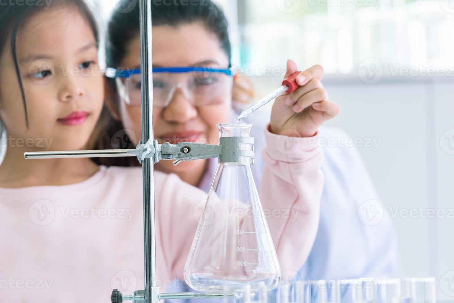 menina cientista e professora soltando pipeta de líquido de substância de solução foto