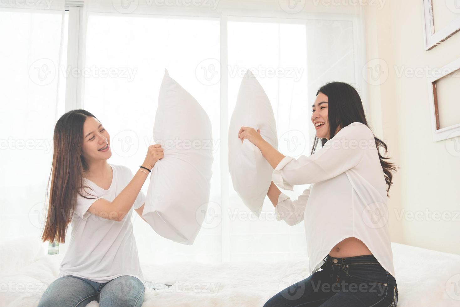 duas garotas asiáticas fazendo guerra de travesseiros no quarto durante a infância foto