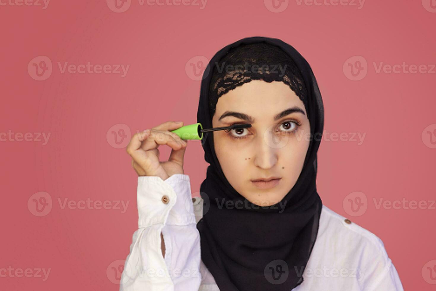 fofa 20s fêmea aplicando rímel inventar. lindo persa mulher tintas dela cílios. atraente meio Oriental mulher dentro hijab fazendo Maquiagem foto