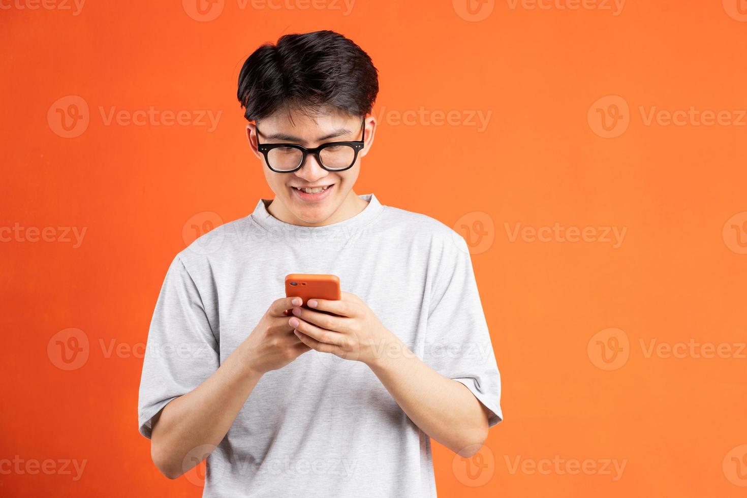 jovem asiático alegre usando telefone isolado em fundo laranja foto