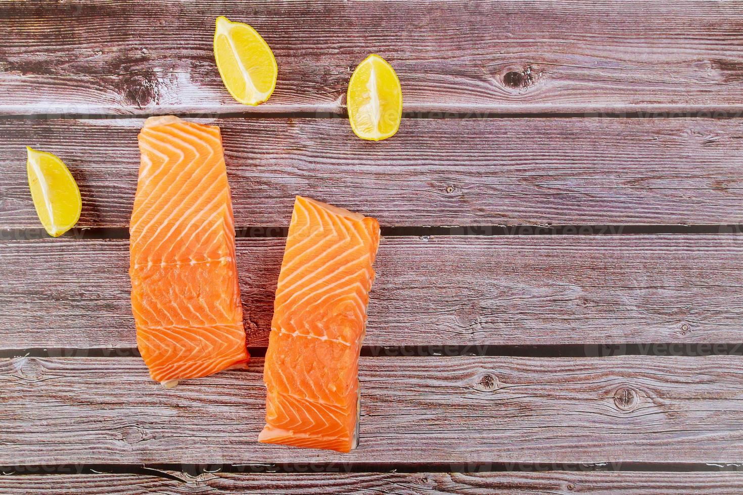 delicioso peixe filé de salmão cru com rodelas de limão na tábua de madeira foto