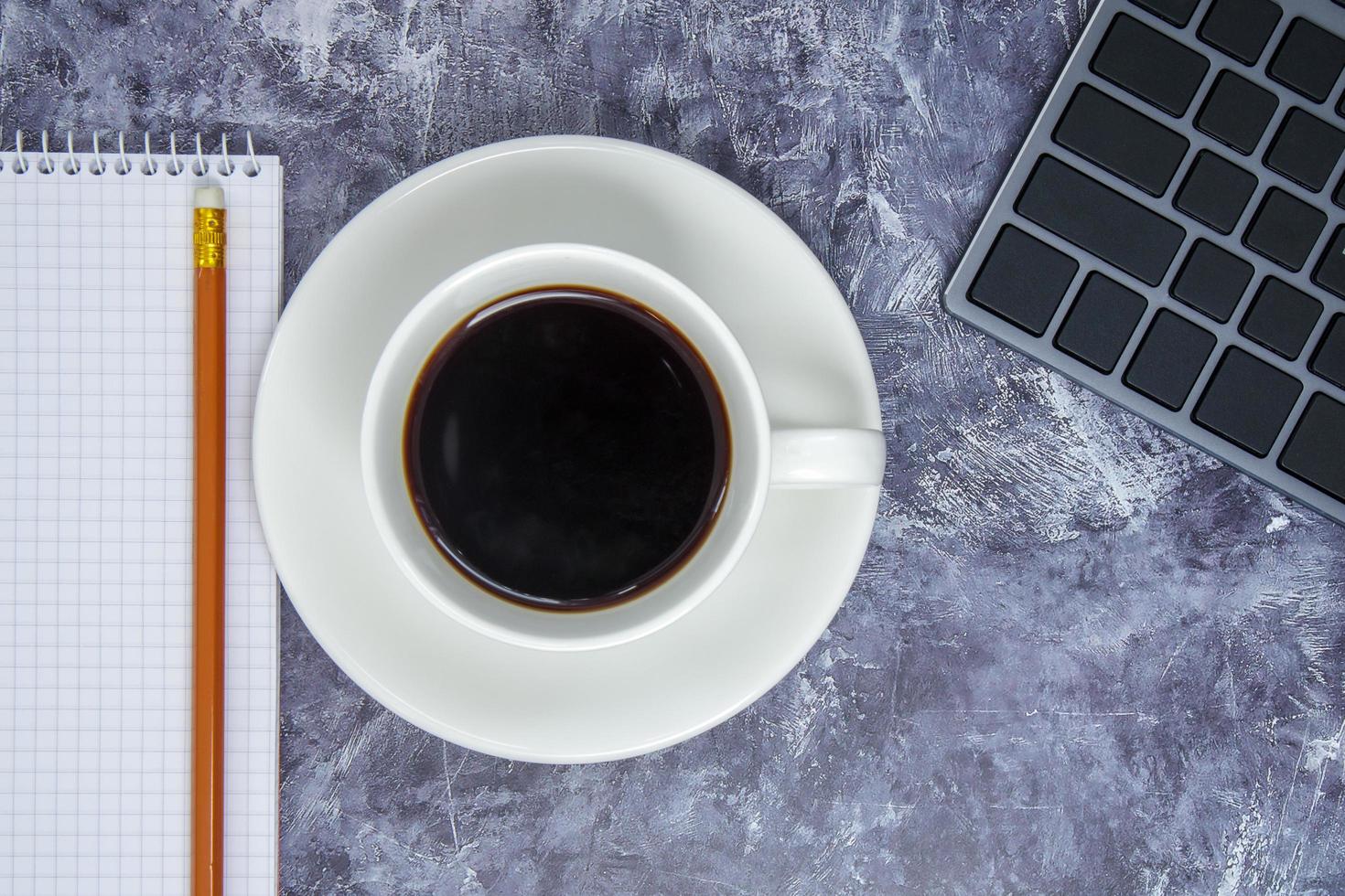 espaço de trabalho com teclado, papelaria, lápis, bloco de notas e xícara de café foto