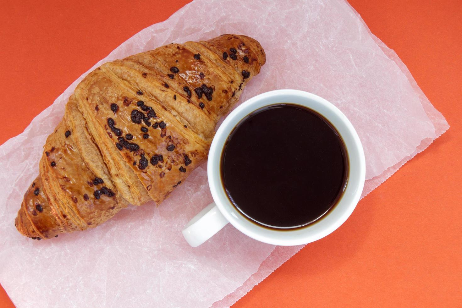 café preto sem leite em uma xícara branca e um croissant de chocolate foto