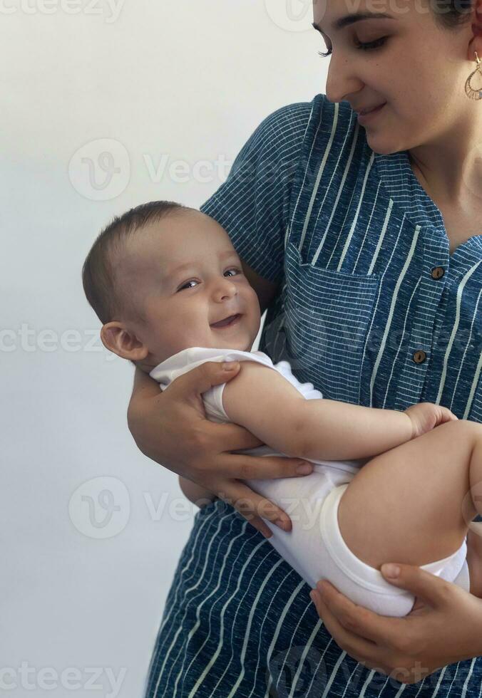 mãe e bebê. mãe segurando dela 6 meses bebê garoto. lindo bebê Garoto do seis meses dentro dele mãe mãos. jovem meio Oriental mãe segurando dentro dela braços dela pequeno filho foto