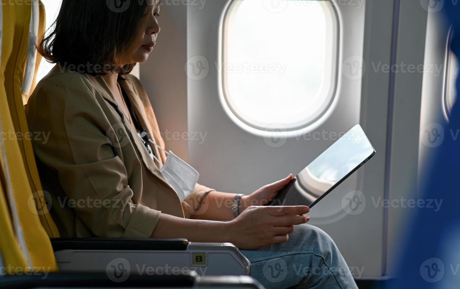 uma viajante usa um tablet durante um vôo de avião. foto
