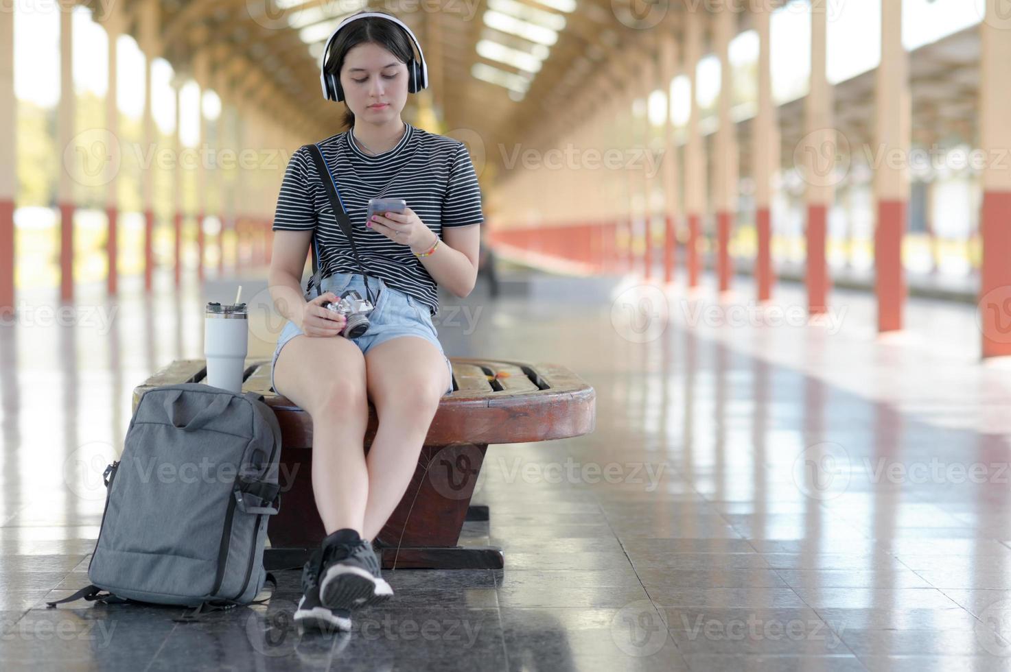 uma jovem viajante ouve música com fones de ouvido enquanto espera por sua jornada na plataforma. foto