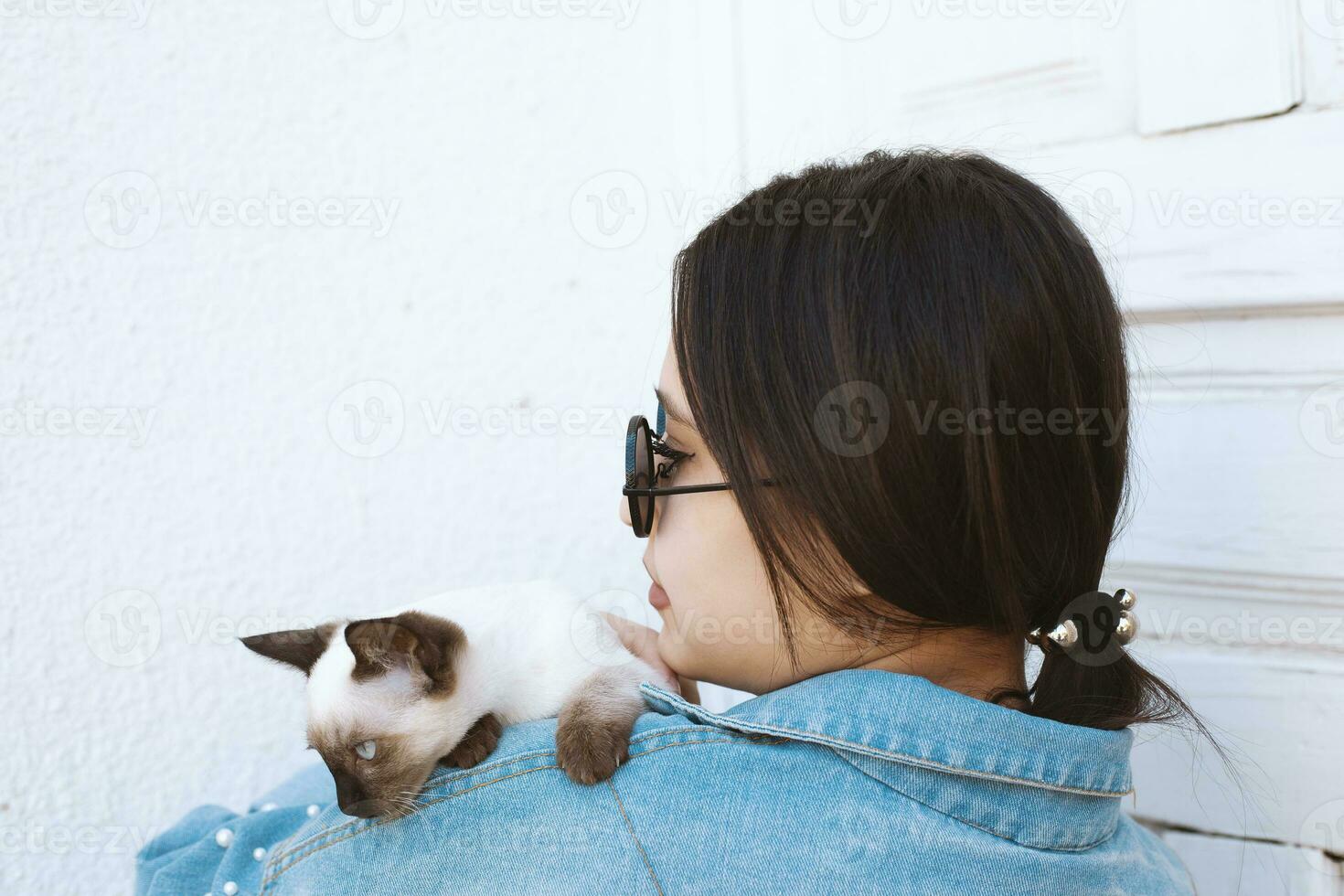 jovem atraente mulher abraçando bichano gato dentro mãos. fofa e glamouroso menina dentro na moda oculos de sol posando com dela siamês gato foto