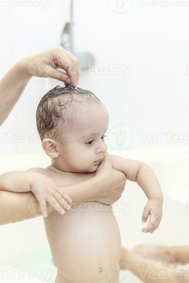 jovem mãe lavando dela bebê Rapazes cabelo às banheiro. mãe tomando banho dela bebê foto