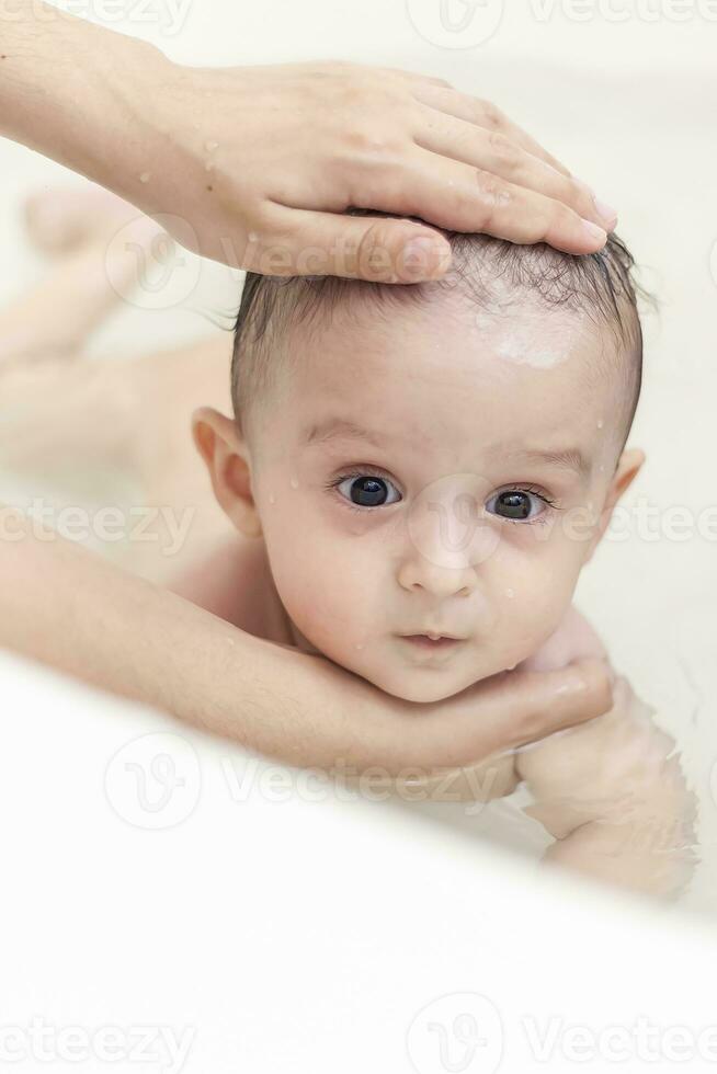 jovem mãe lavando dela bebê Rapazes cabelo às banheiro. mãe tomando banho dela bebê foto