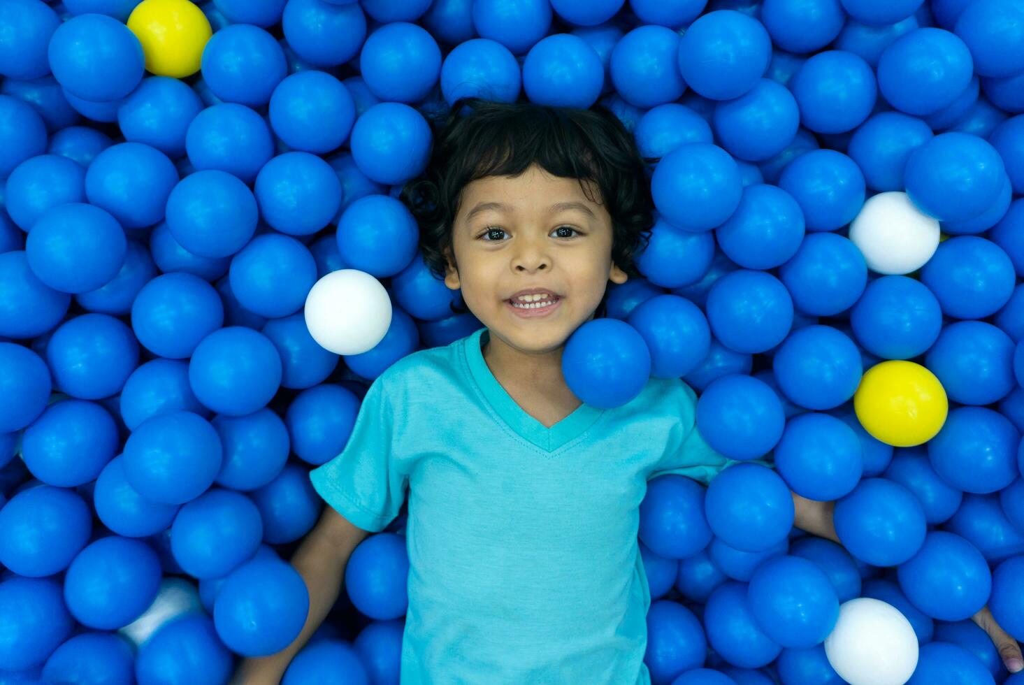 uma pequeno ásia Garoto é jogando com uma muitos do azul e amarelo bolas foto