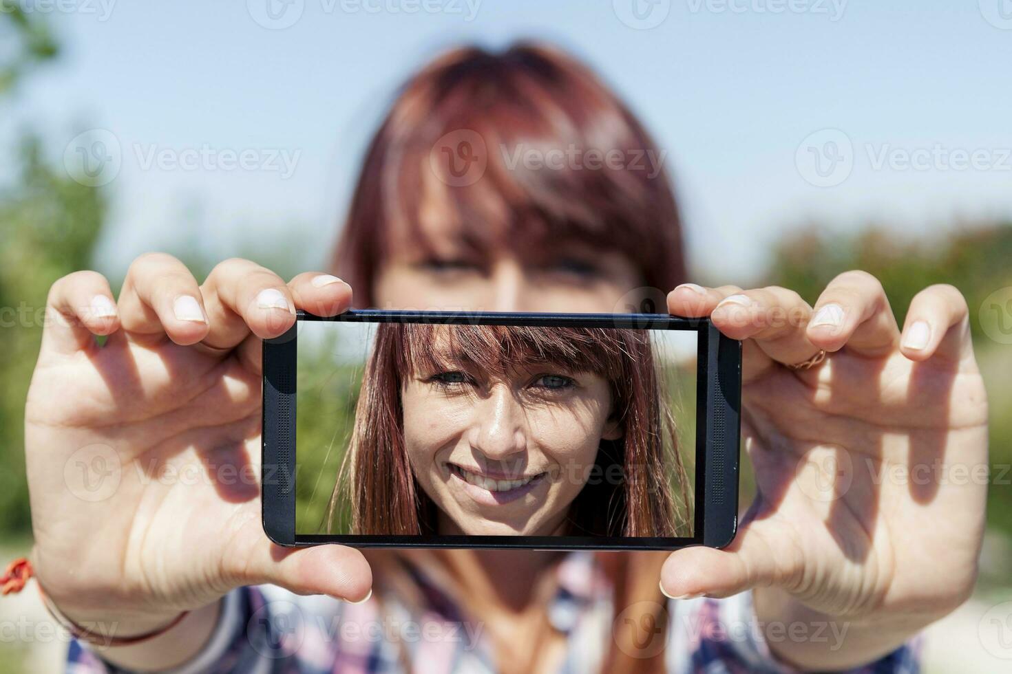 bonita mulher com vermelho cabelo levar uma selfie com inteligente telefone foto