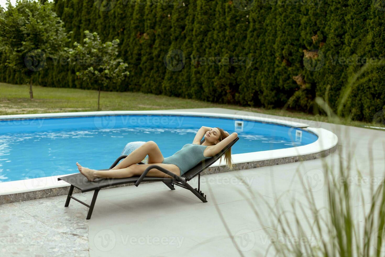 jovem deitada em um deck char à beira da piscina no quintal da casa foto