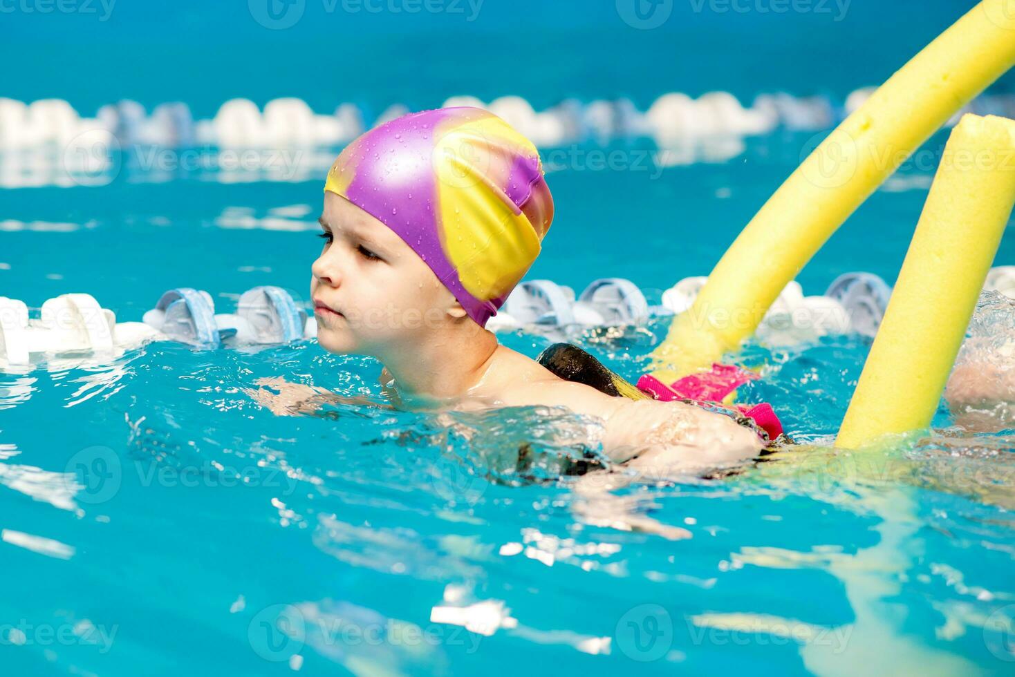uma pequeno Garoto com uma vida Jaqueta em dele peito aprende para nadar dentro a interior piscina. foto