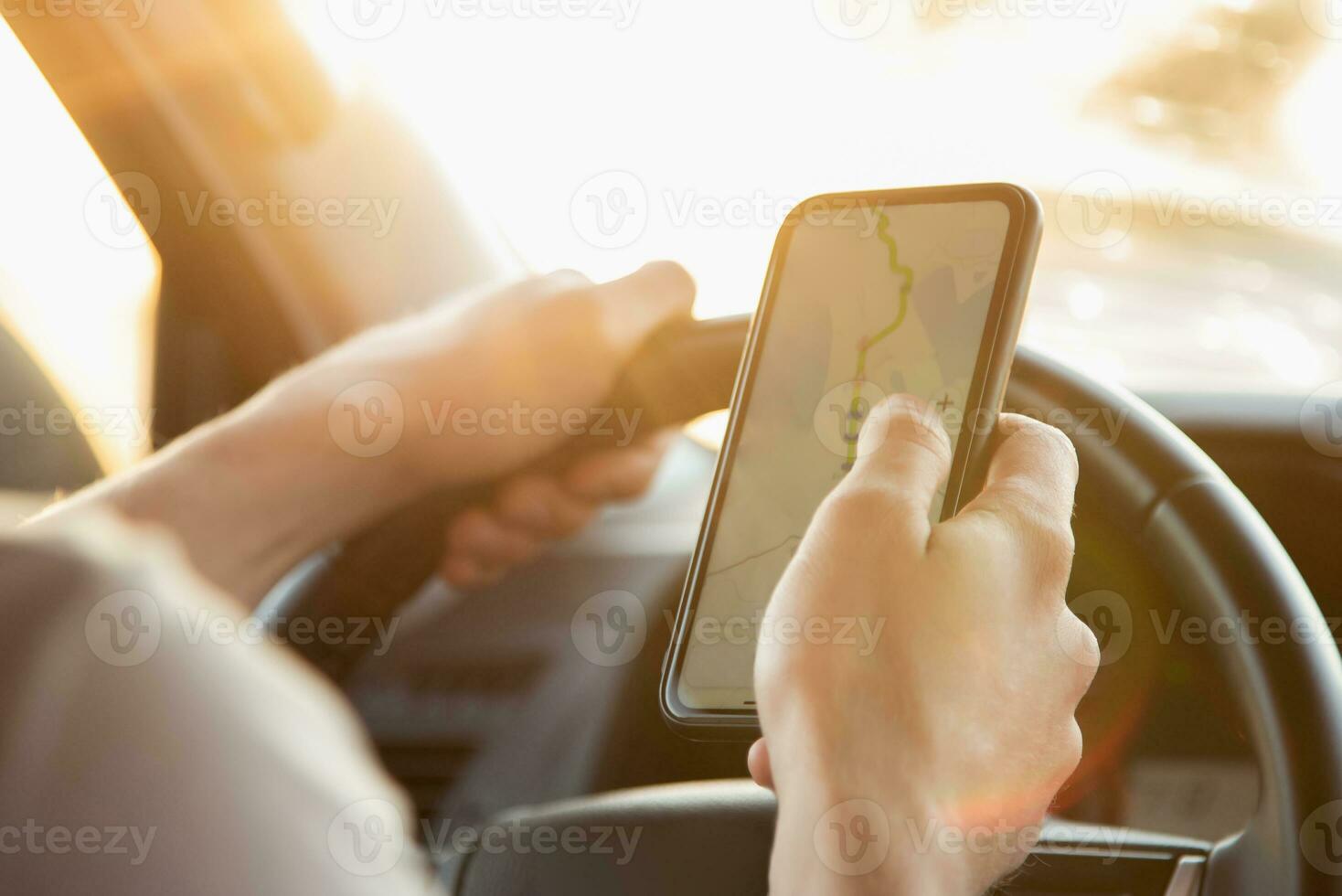 uma homem senta dentro uma carro e parece às dele telefone com a navegador aplicativo em uma ensolarado dia foto