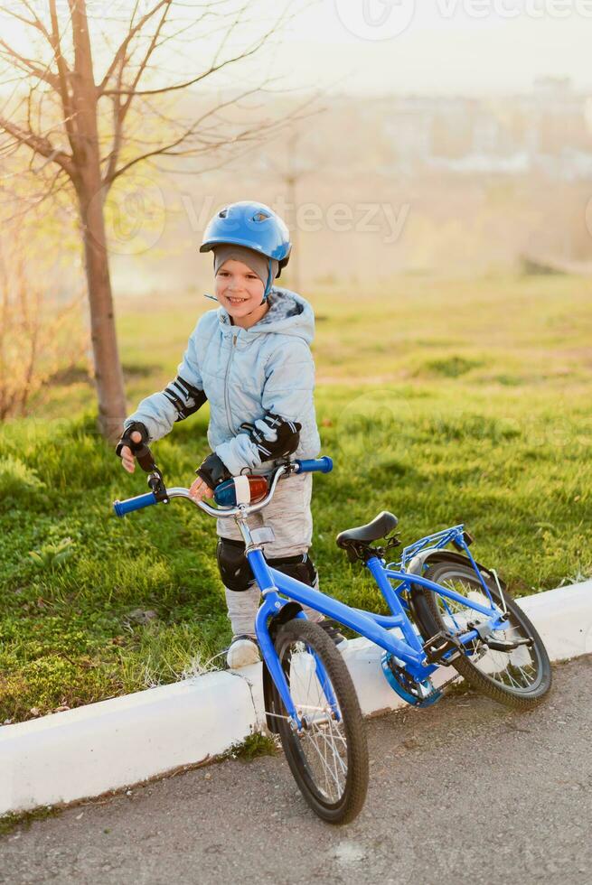 uma criança dentro uma capacete aprende para passeio uma bicicleta em uma ensolarado dia às pôr do sol foto