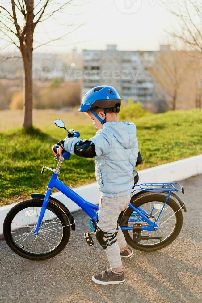 uma criança dentro uma capacete aprende para passeio uma bicicleta em uma ensolarado dia às pôr do sol foto