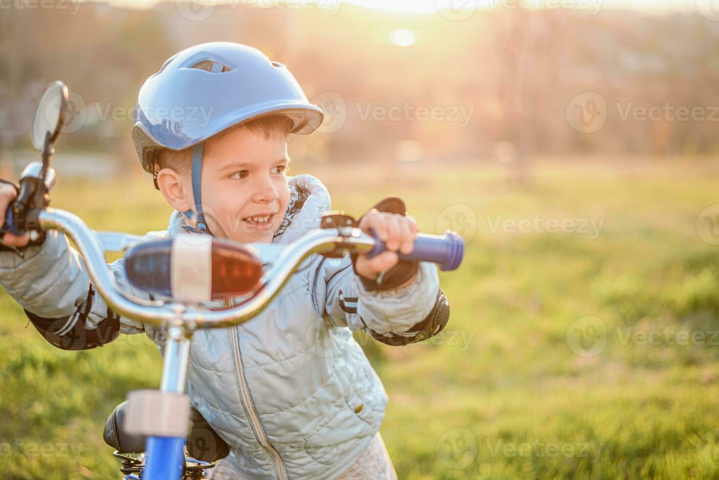 fofa criança é dirigindo uma bicicleta em uma ensolarado dia às pôr do sol foto