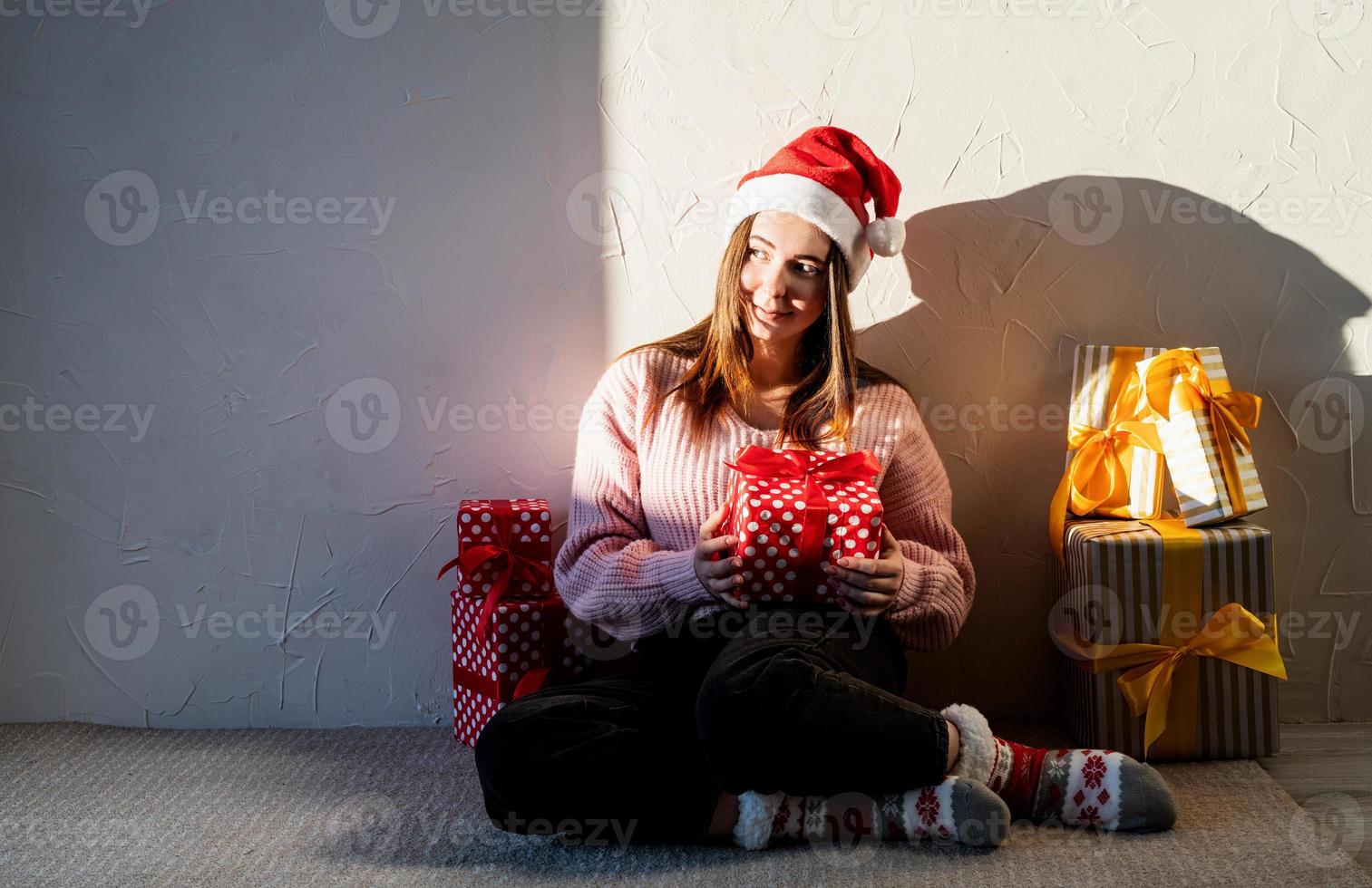 jovem com chapéu de Papai Noel cercada de presentes foto