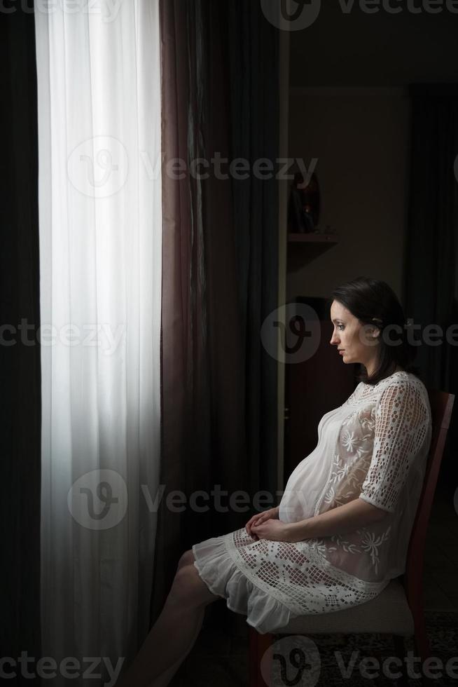 mulher grávida sentada perto de uma janela foto