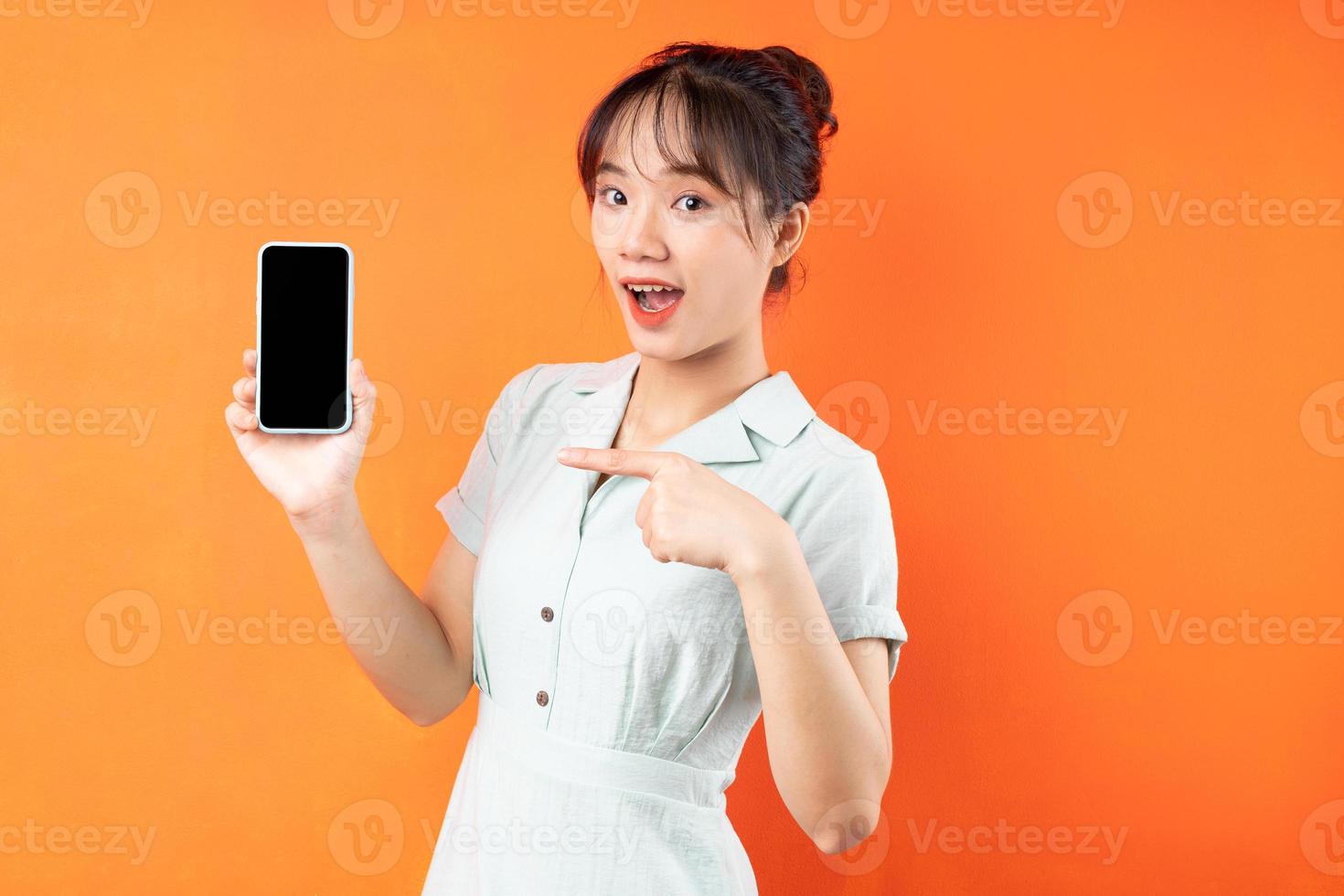 retrato de jovem mostrando a tela do telefone, isolado em um fundo laranja foto
