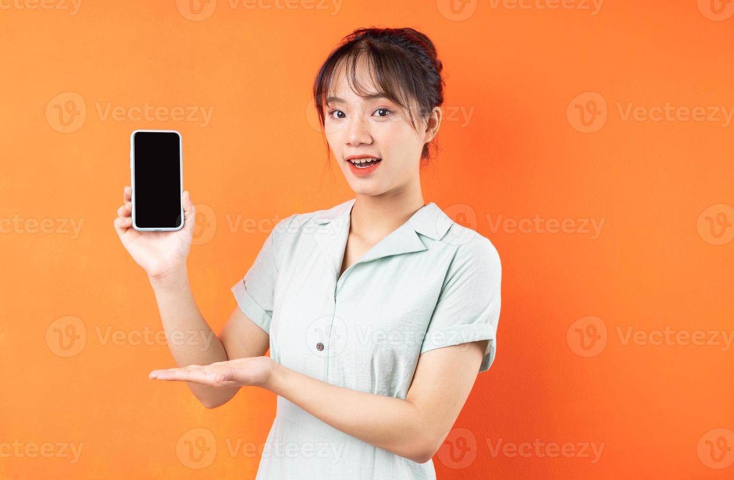 retrato de jovem mostrando a tela do telefone, isolado em um fundo laranja foto