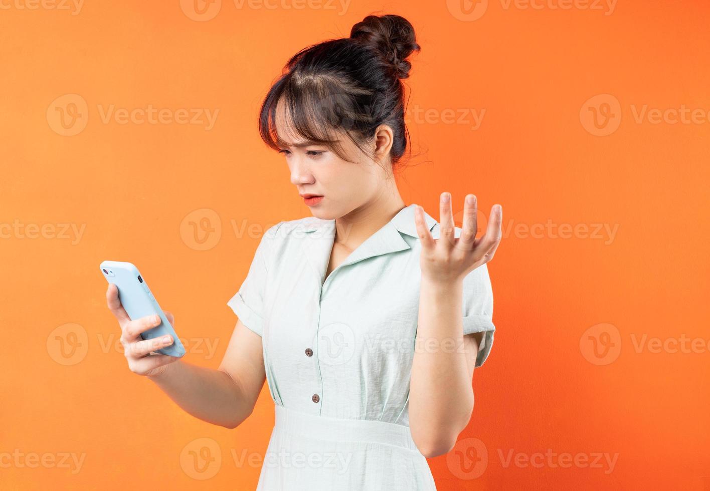 retrato de jovem usando telefone e se sentindo irritada, isolado em um fundo laranja foto