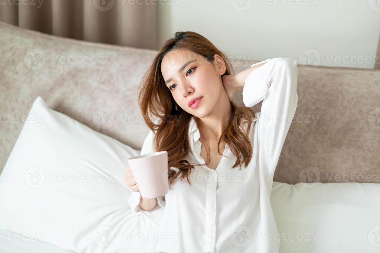 retrato de mulher bonita acordar e segurando uma xícara de café ou caneca na cama foto