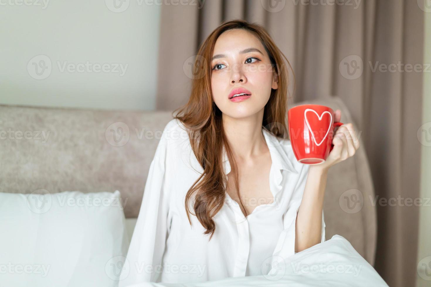 retrato de mulher bonita acordar e segurando uma xícara de café ou caneca na cama foto