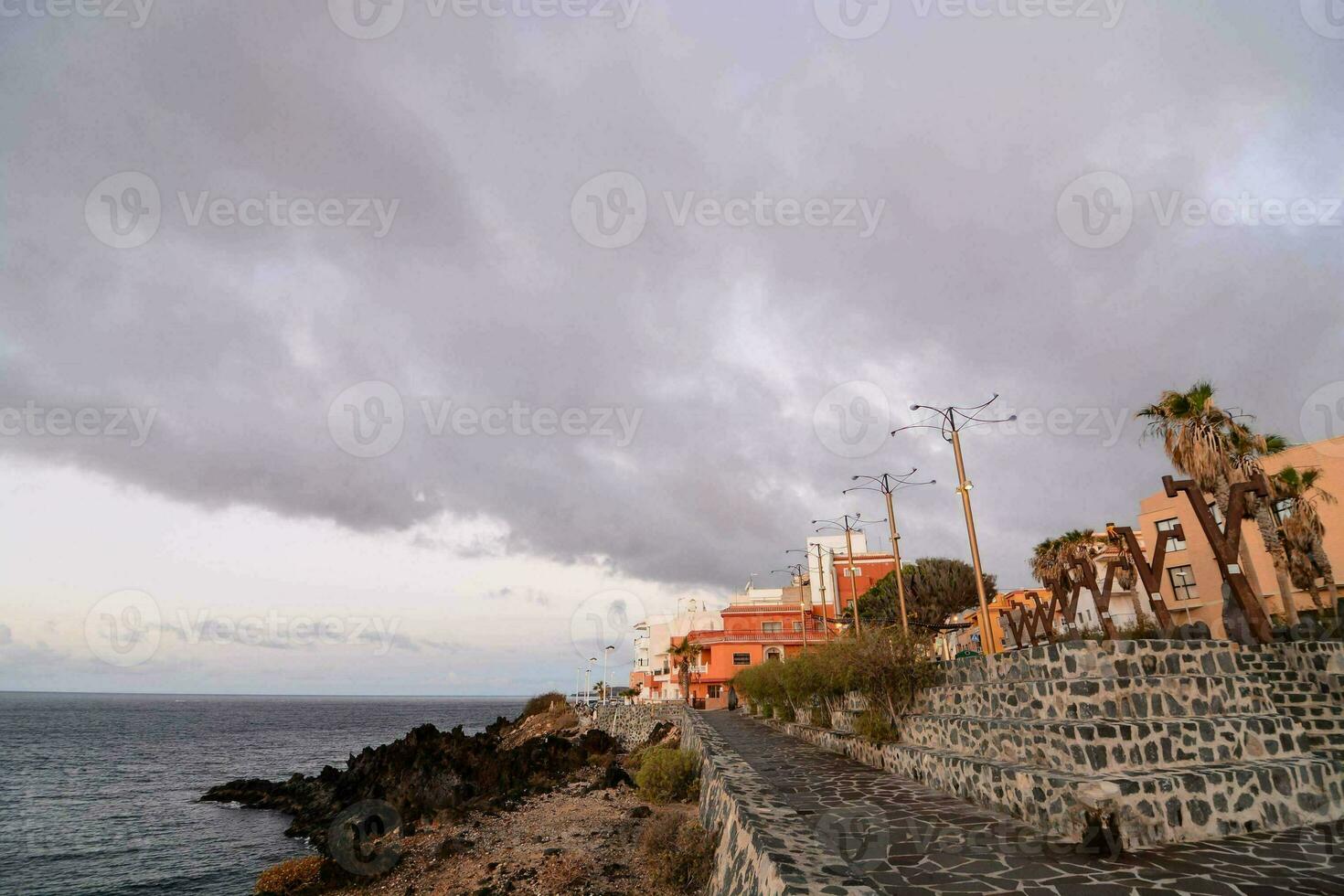 uma rochoso caminho conduz para a oceano e edifícios foto