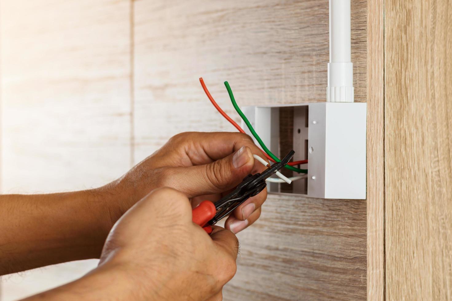 eletricista está removendo fios elétricos em uma caixa de plástico em uma parede de madeira para instalar a tomada elétrica. foto