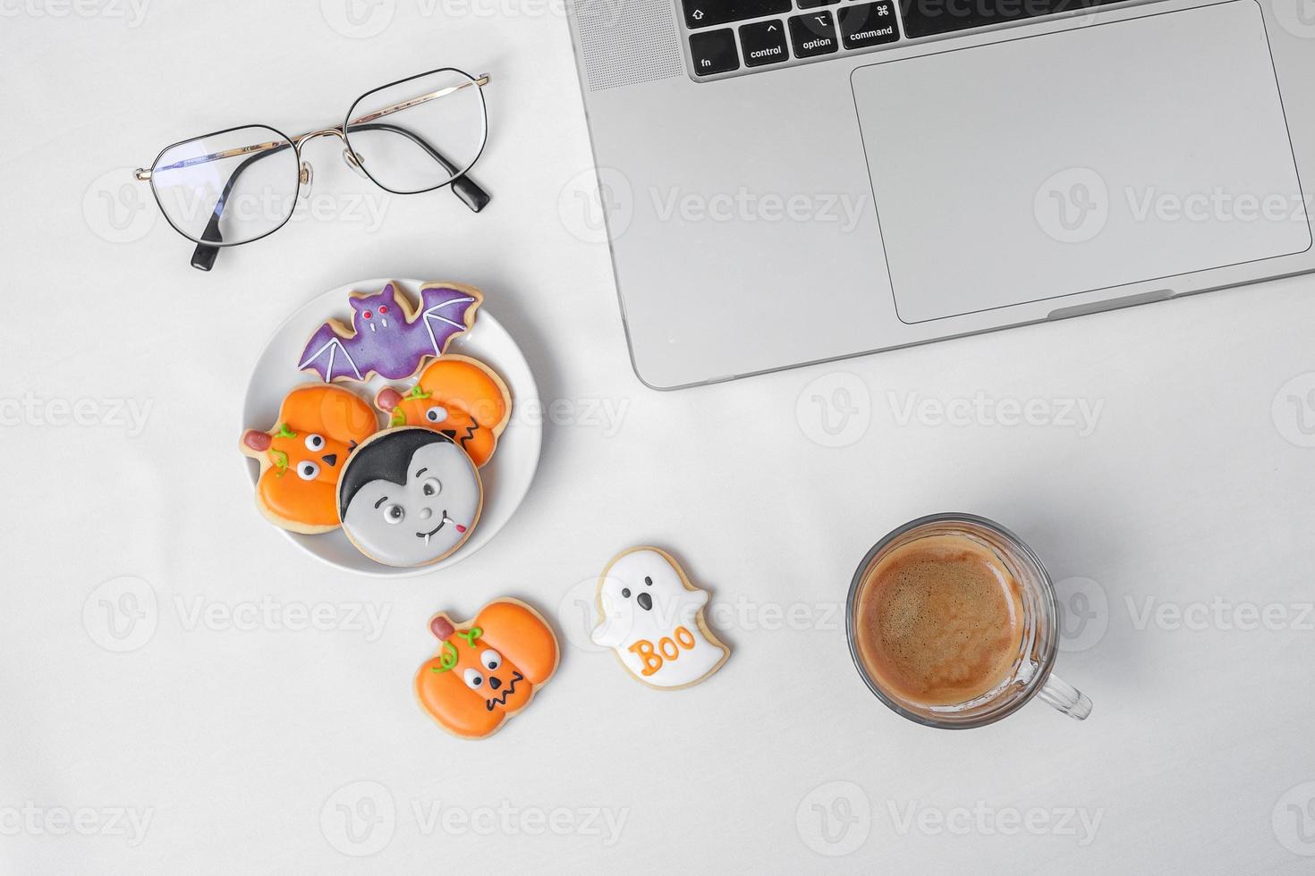 biscoitos de halloween, café quente e computador portátil em fundo branco. feliz dia das bruxas, compras online, olá outubro, outono outono, festivo, festa e conceito de férias foto